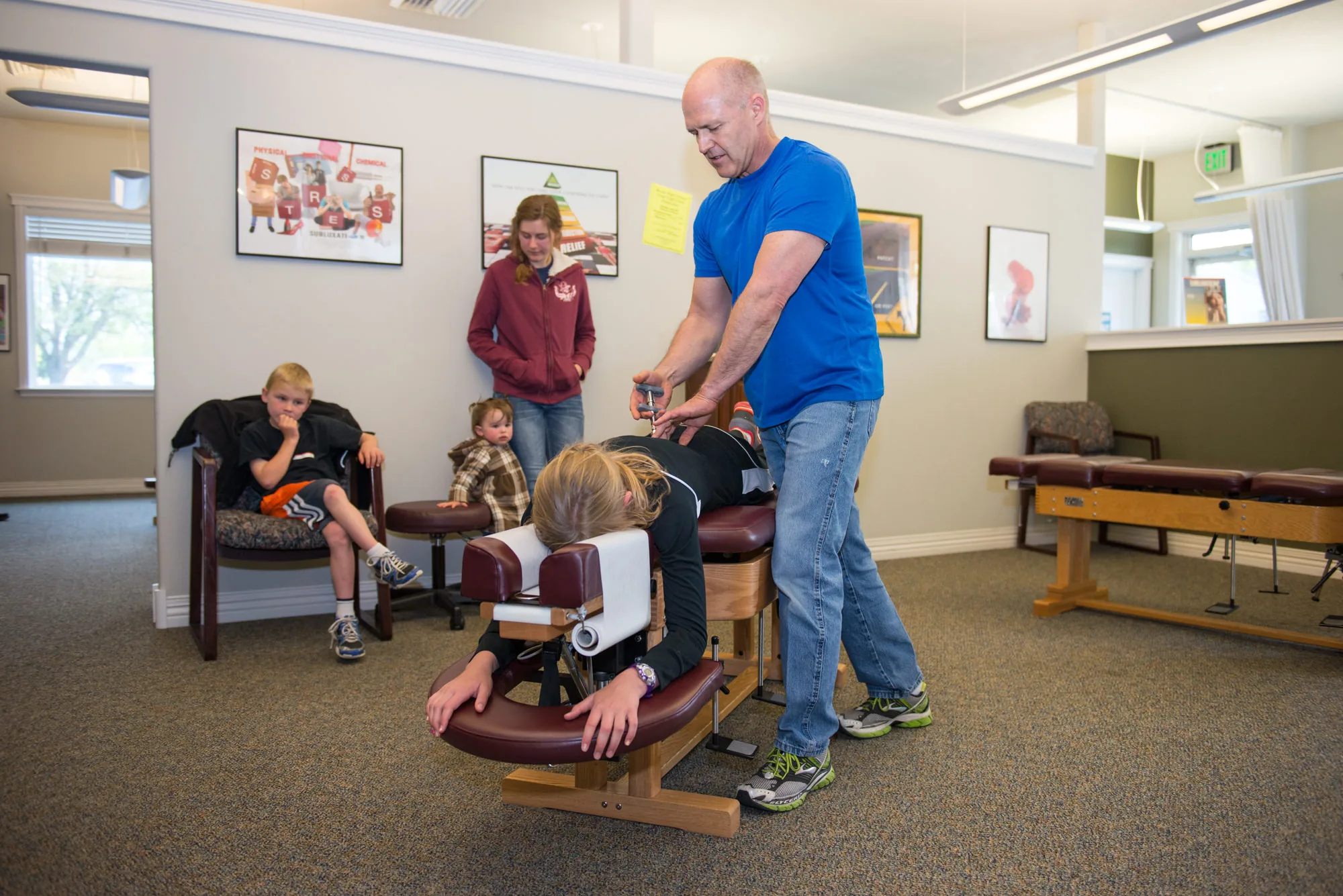 Chiropractor adjusting a child patient on a treatment table while family members watch in a clinic.