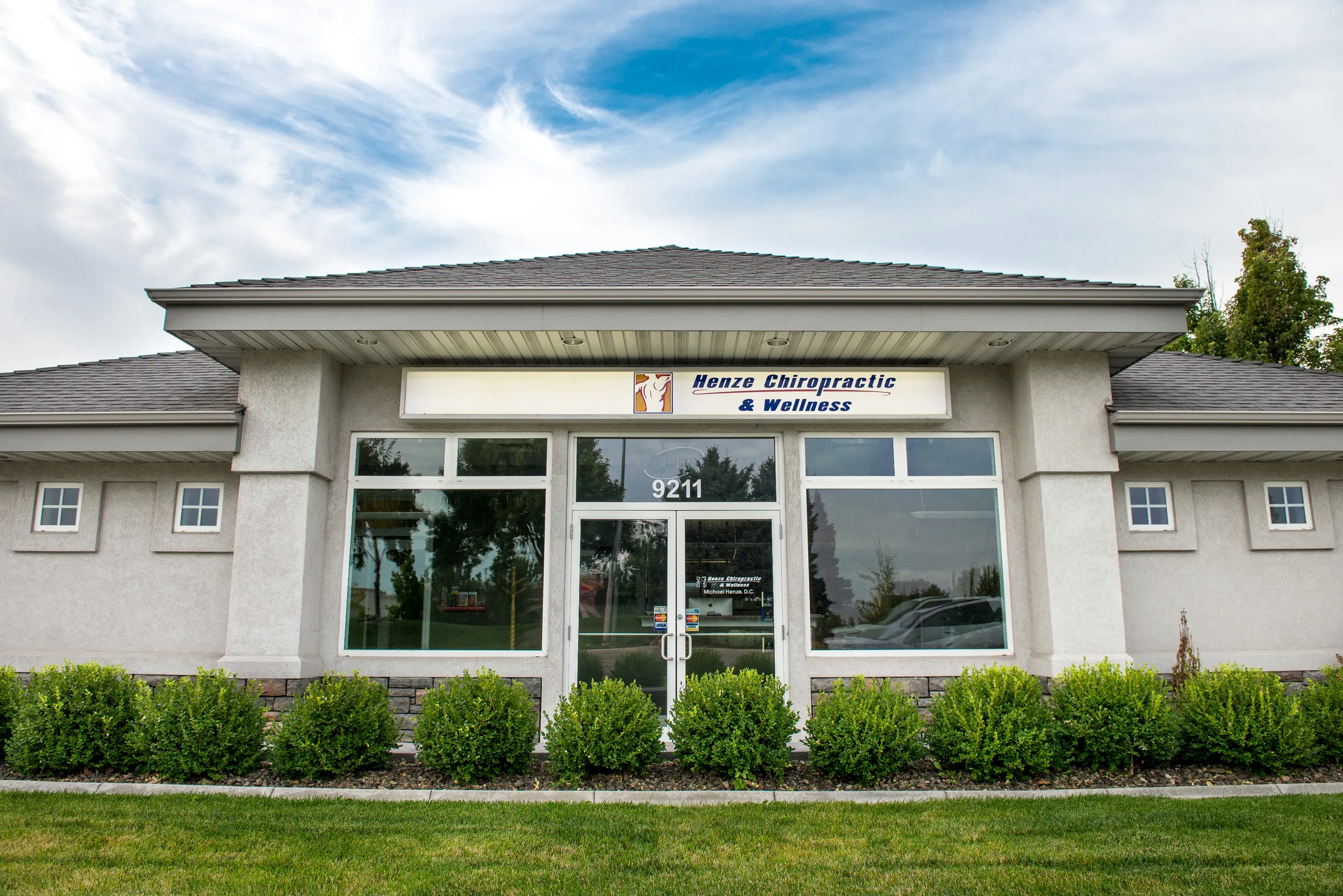 Exterior of Henze Chiropractic and Wellness clinic building with address 9211 and landscaping.
