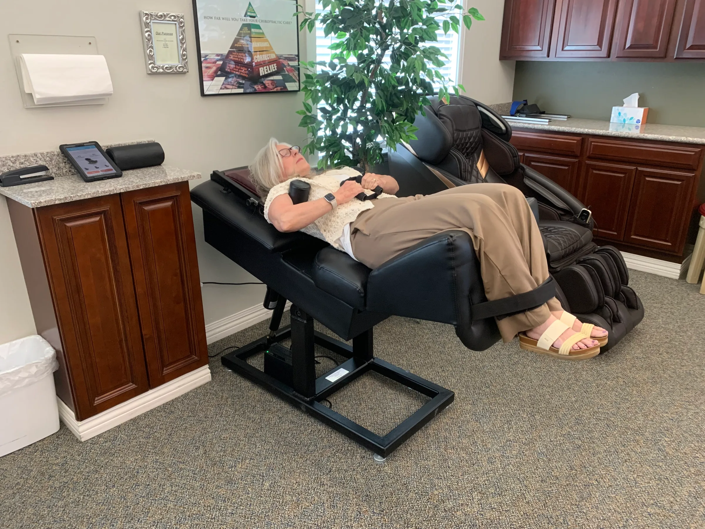 Patient relaxing in a black massage chair at a chiropractic wellness office.